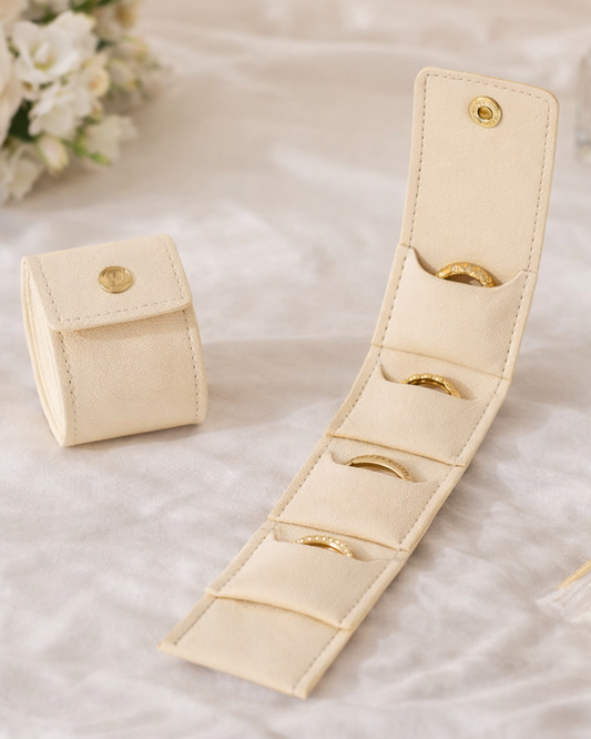 Beige jewelry organizer with rings on a soft surface with flowers and a bottle in the background