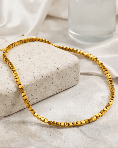 Gold necklace on a textured surface with a glass of water in the background