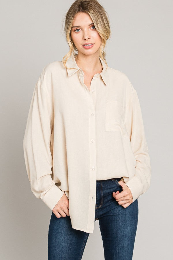 Woman wearing a beige button-up shirt and blue jeans on a gray background