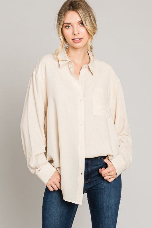 Woman wearing a beige button-up shirt and blue jeans on a gray background
