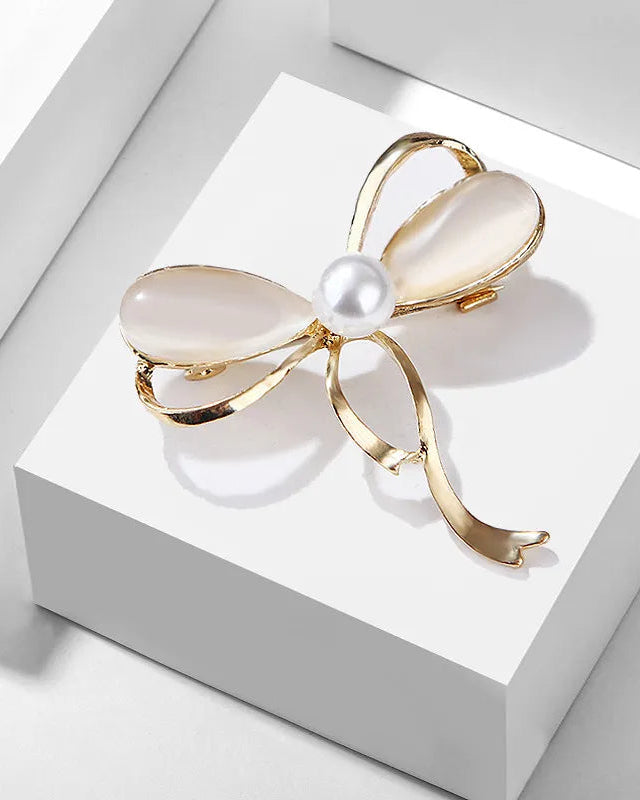Gold bow-shaped brooch with a pearl center on a white box