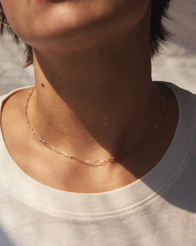 Person wearing a delicate gold necklace against a neutral background