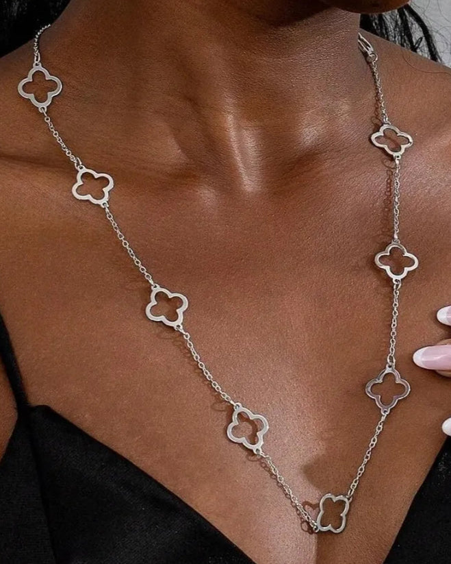 Woman wearing a silver necklace with clover-shaped pendants against a neutral background