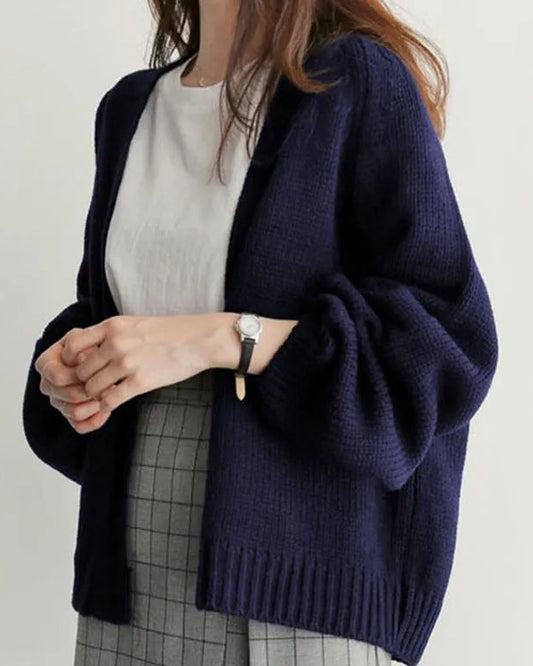 Person wearing a navy blue cardigan over a white shirt and plaid skirt on a plain background