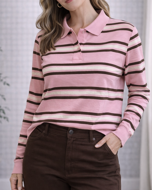 Woman wearing a pink and brown striped sweater with brown pants indoors.