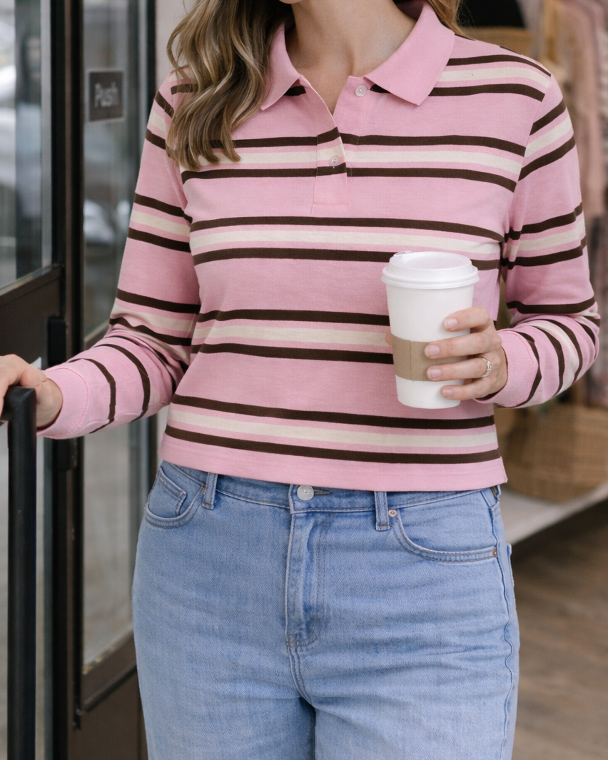 Woman wearing a pink and brown striped sweater holding a coffee cup in a store setting.