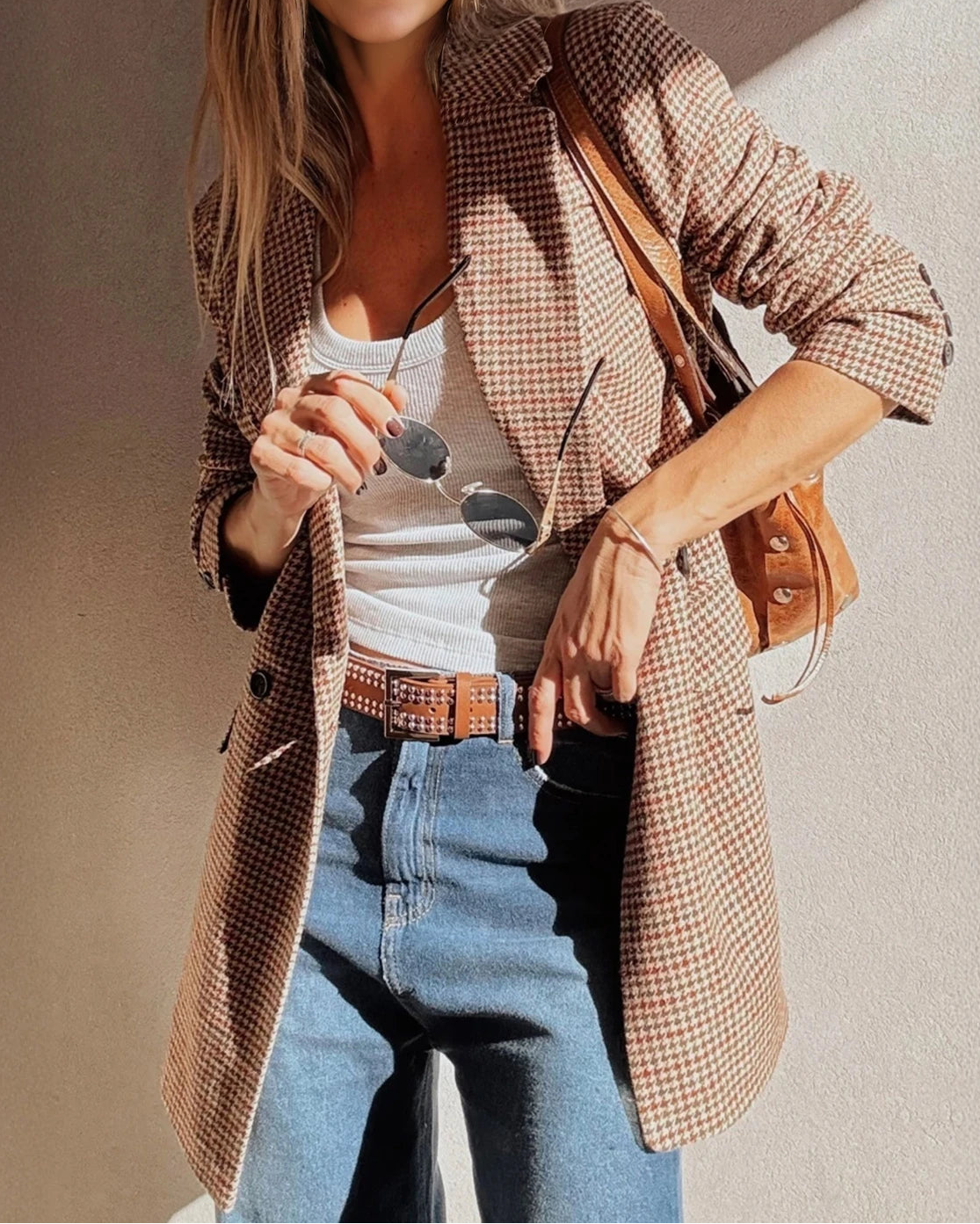 Woman wearing a plaid jacket, white top, and blue jeans with a brown leather bag.