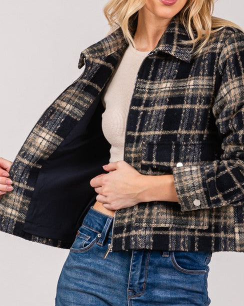 Woman wearing a plaid jacket over a white shirt and blue jeans on a plain background