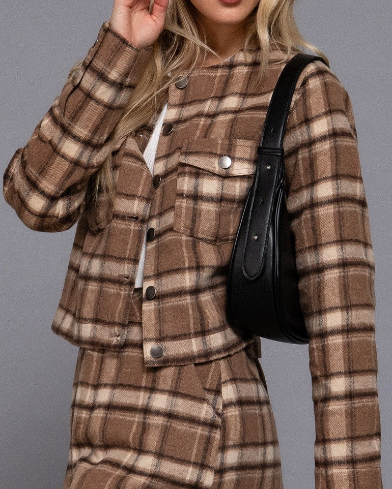 Woman wearing a brown plaid dress with a black handbag against a gray background