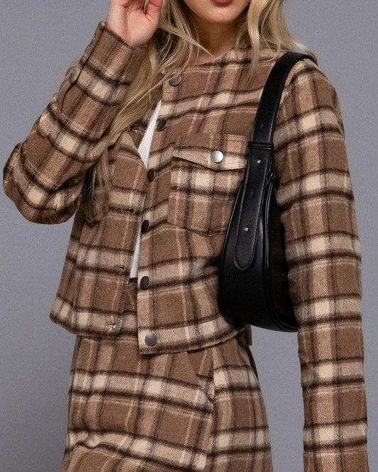 Woman wearing a brown plaid dress with a black handbag against a gray background