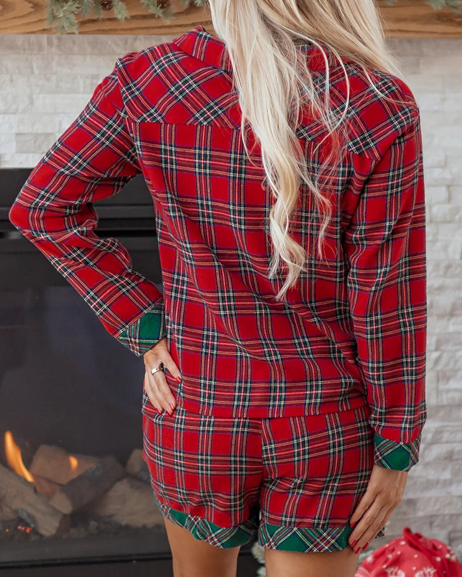 Person wearing a red plaid pajama set in front of a fireplace with Christmas decorations.