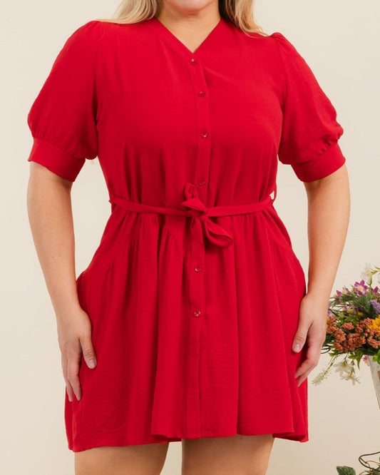Woman wearing a red dress standing in front of a decorative background with flowers and plants.