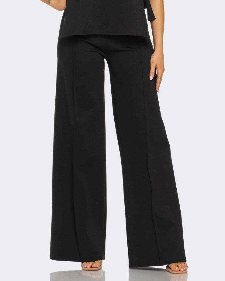 Woman wearing a black sleeveless top and wide-leg pants on a white background