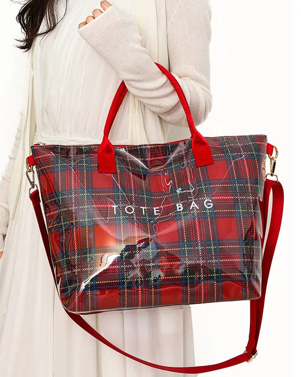 A woman in a white dress holds a red plaid tote bag with a transparent front panel and red handles. The bag has a white printed 'TOTE BAG' text and a red shoulder strap.
