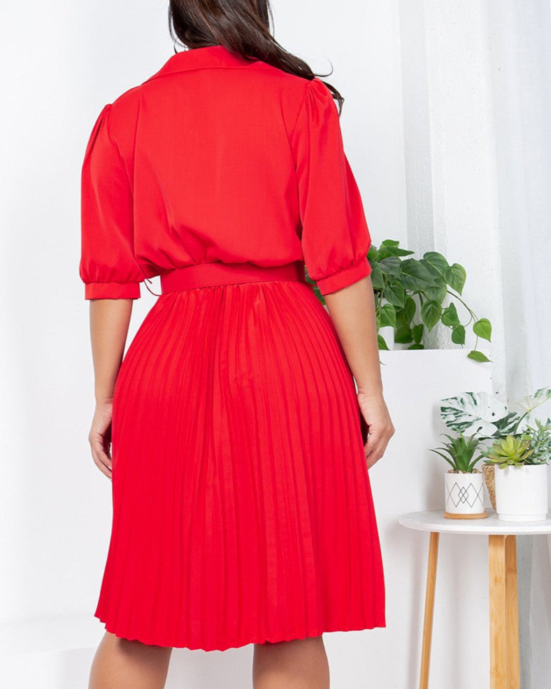 Woman wearing a red dress standing in a room with a white wall and a small table with plants.