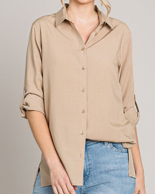 Woman wearing a beige button-up shirt and blue jeans against a plain background