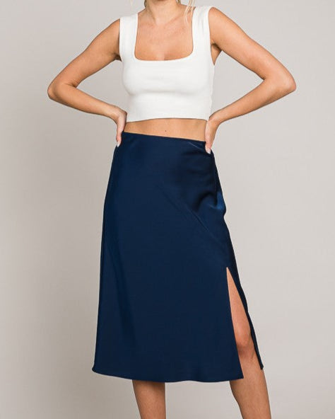 Woman wearing a white crop top and navy skirt on a plain background