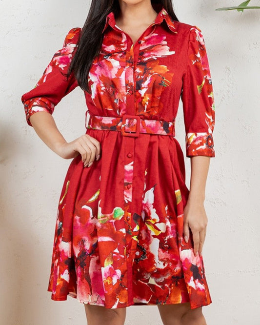 Woman wearing a red floral dress standing indoors with plants in the background