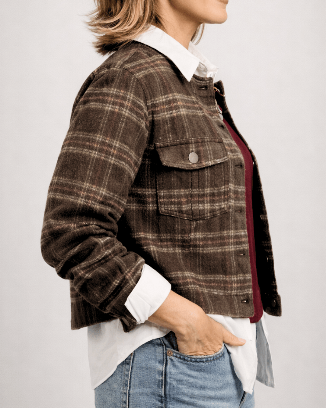 Person wearing a brown plaid jacket over a white shirt with a neutral background