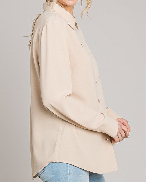 Woman wearing a beige blazer and light blue jeans against a plain background