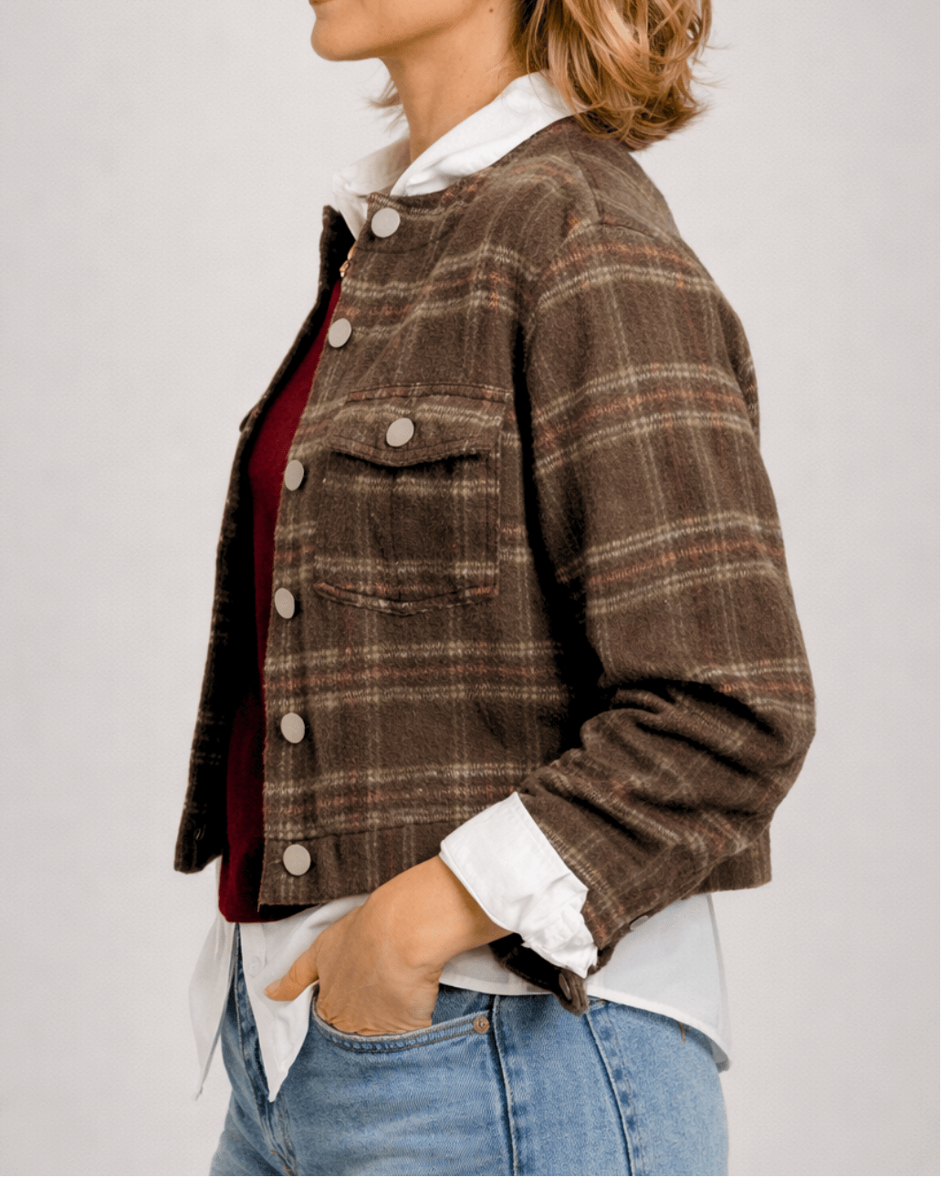Person wearing a brown plaid jacket with a plain background