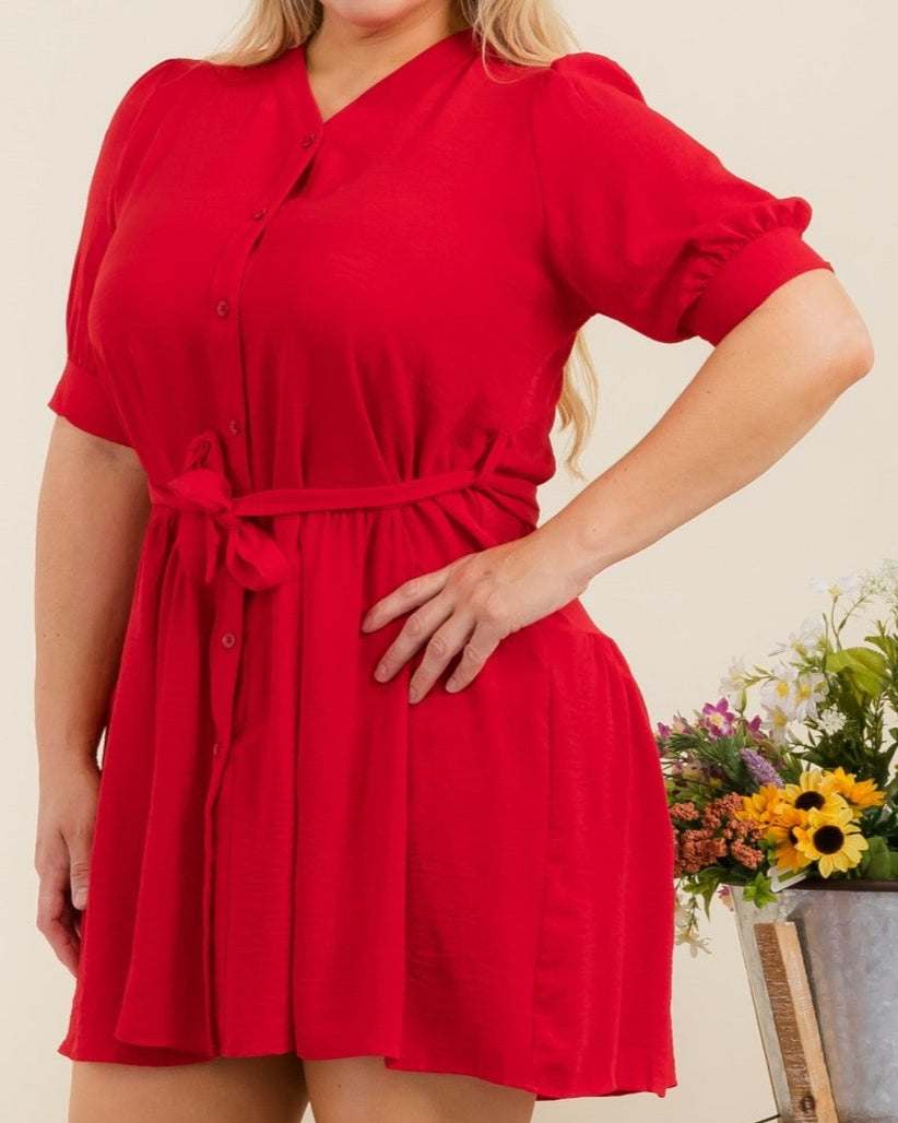 Woman wearing a red dress standing next to a plant and decorative items.