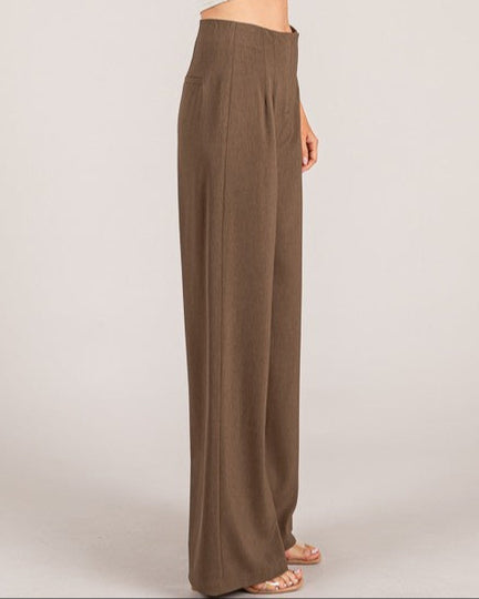 Woman wearing a white top and brown wide-leg pants on a plain background
