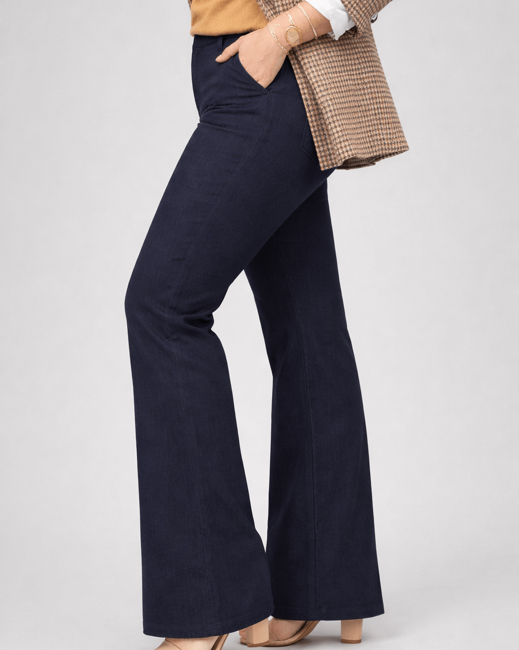 Person wearing navy flared pants with a beige jacket on a light gray background