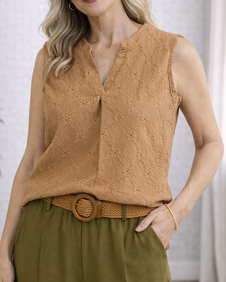 Woman wearing a brown sleeveless top and green pants indoors.
