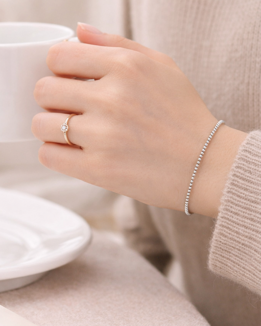Hand holding a teacup with a silver ring and bracelet on a neutral background
