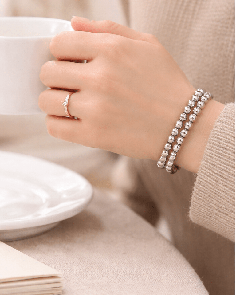 Hand wearing a silver bracelet and ring, holding a white cup with a blurred background