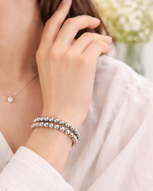 Close-up of a person wearing a silver bracelet and necklace, with a blurred background.