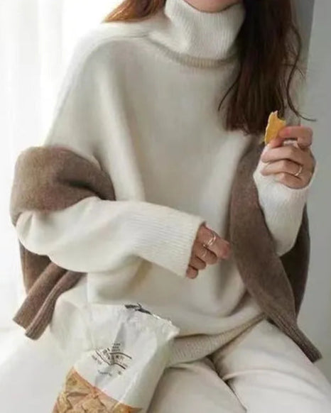 Person wearing a white turtleneck sweater with brown accents, sitting on a windowsill.