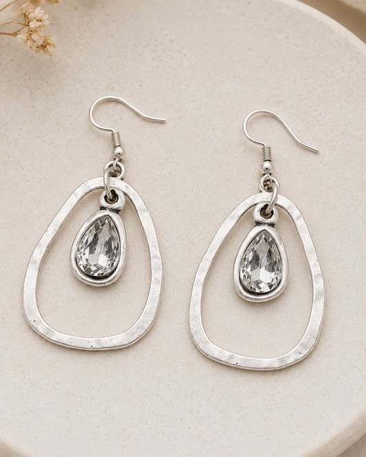 Silver teardrop earrings on a beige plate with dried flowers.
