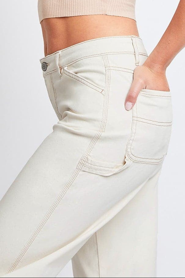 Woman wearing a beige crop top and white jeans on a light gray background