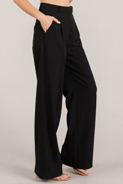 Woman wearing a white tank top and black wide-leg pants on a plain background
