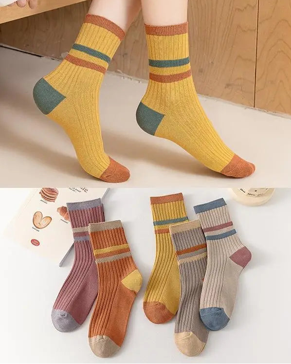 Colorful socks with striped patterns worn by a person, displayed against a wooden floor.